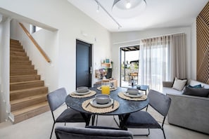 A modern living room with a dining area, a staircase, and a view to the outside.