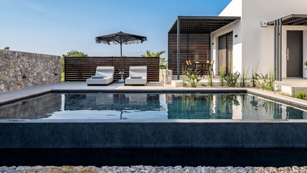A modern outdoor pool area with a stone wall, two lounge chairs, and a pergola. - Campo Premium Villa with Private Pool (Kos)