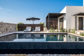 A modern outdoor pool area with a stone wall, two lounge chairs, and a pergola. - Campo Premium Villa with Private Pool (Kos)