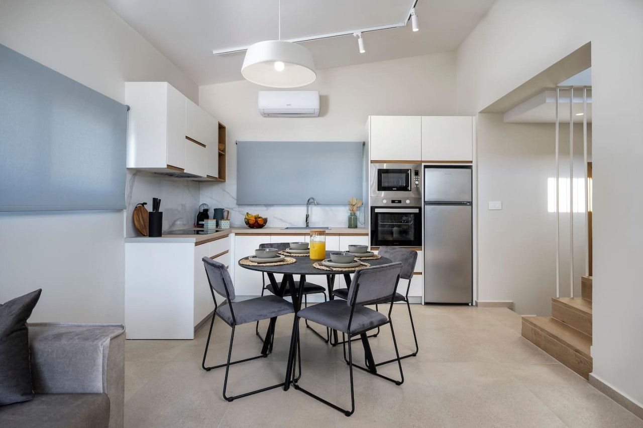 Een moderne keuken met witte kasten, een eettafel met stoelen en een inbouwoven.
