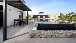 Un patio al aire libre con una mesa y sillas de comedor, una pared de piedra y una zona de piscina.