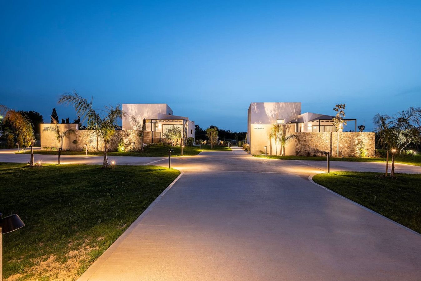 A modern residential area with two houses, a paved driveway, and well-maintained landscaping.