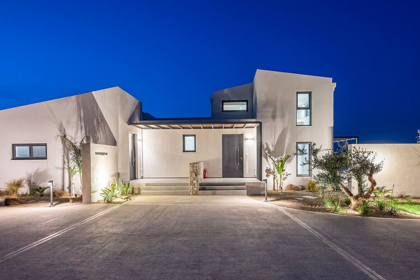 Une maison moderne à deux étages, dotée d’un toit plat, d’un porche et d’une allée bien éclairée.