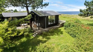 Een moderne chalet met terras, omgeven door weelderige begroeiing en uitzicht op een waterpartij.