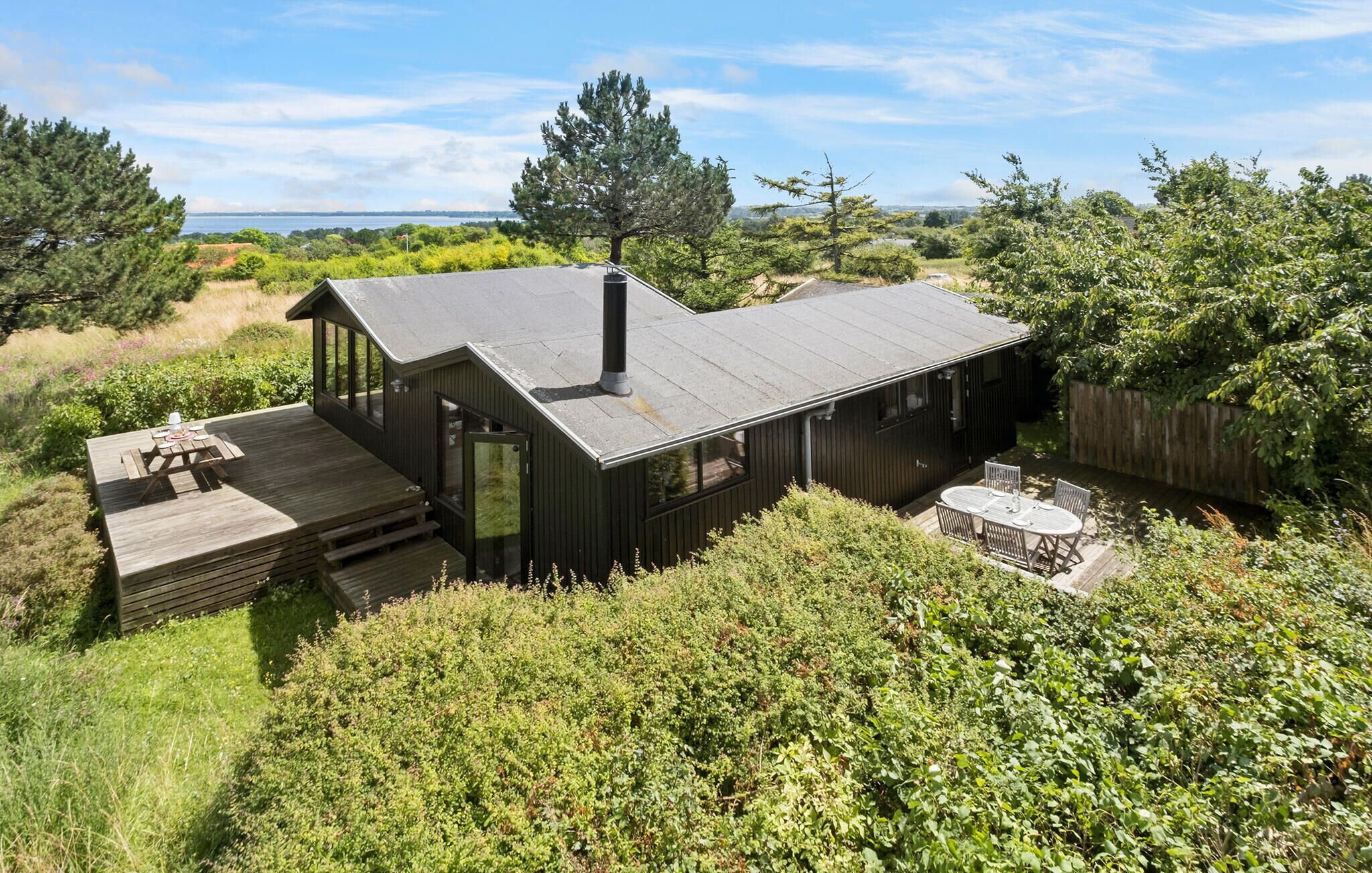 A modern house with a deck, a hot tub, and a view of the sea.