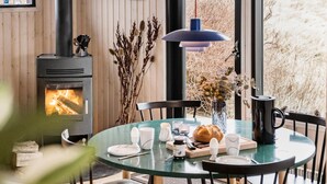 Een gezellig eetgedeelte met een ronde glazen tafel, stoelen, een open haard en uitzicht op de omgeving.