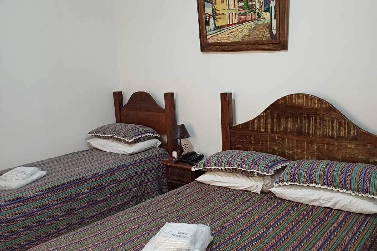 Quarto de hotel com duas camas de solteiro, cada uma com colcha listrada e almofadas combinando. Cada cama tem uma cabeceira de madeira, e um quadro emoldurado está pendurado na parede acima das camas.