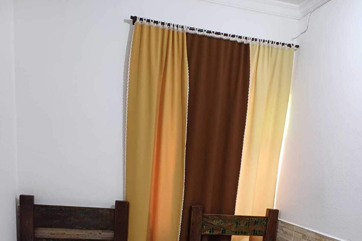 Quarto pequeno com duas camas de solteiro, mesa de cabeceira e janela com cortinas.