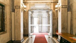 A grand entrance with a red carpet leading to a set of double doors, flanked by tall columns and wall-mounted lighting. - Apartment Togni "y" (Milano)