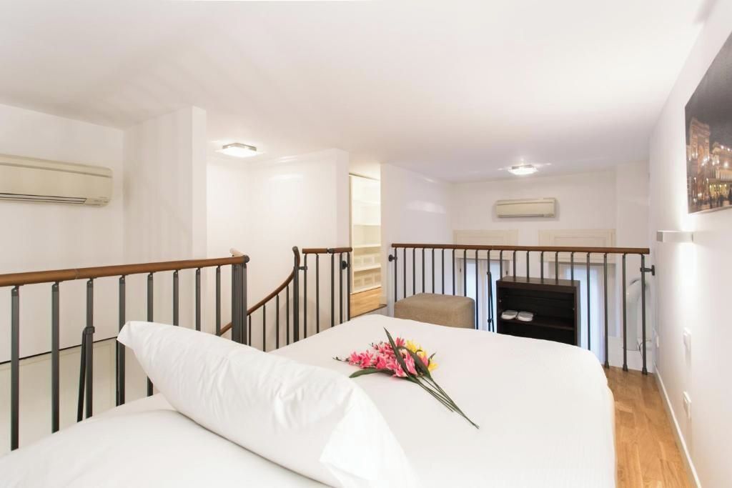 A hotel room with a bed, a wooden railing, a small seating area, and a staircase.