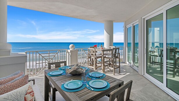 A dining area with a view of the ocean, featuring a wooden table set with blue plates and glasses, and a white ceiling. - Ahh.. The VIEW! · Gulf Front Beauty · Private Beach & Free Beach Service (Santa Rosa Beach)