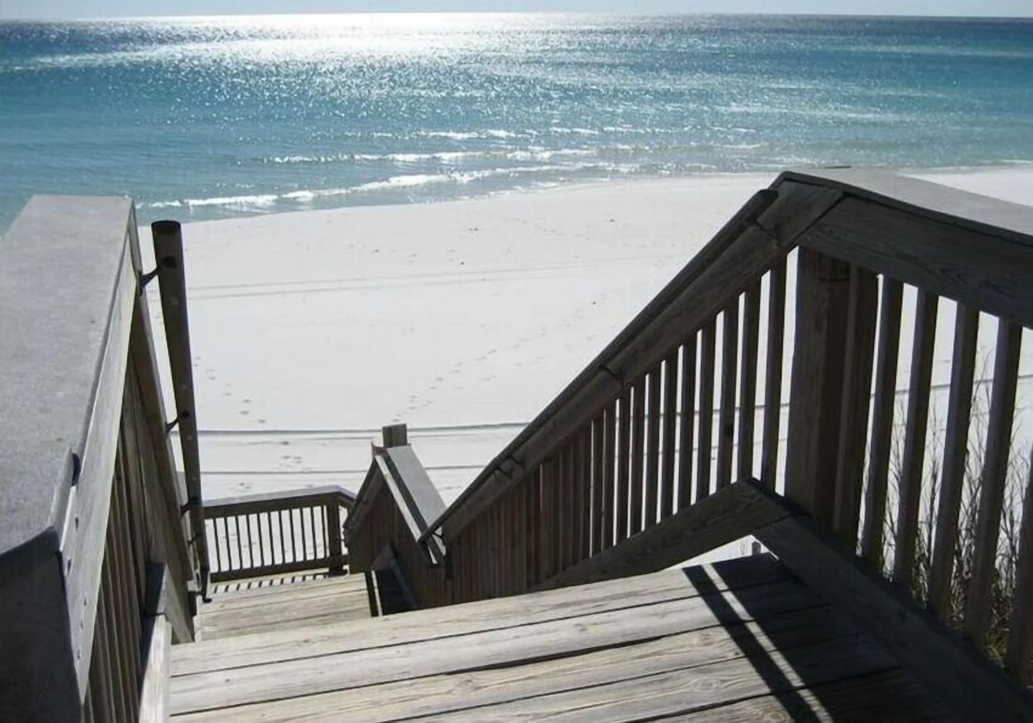A wooden staircase leading to a beach with a clear view of the ocean.