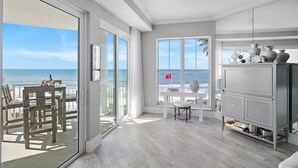 A spacious room with a large sliding glass door leading to a balcony with a view of the ocean. There is a dining area with a table and chairs, and a grey cabinet with decorative items. - Ahh.. The VIEW! · Gulf Front Beauty · Private Beach & Free Beach Service (Santa Rosa Beach)