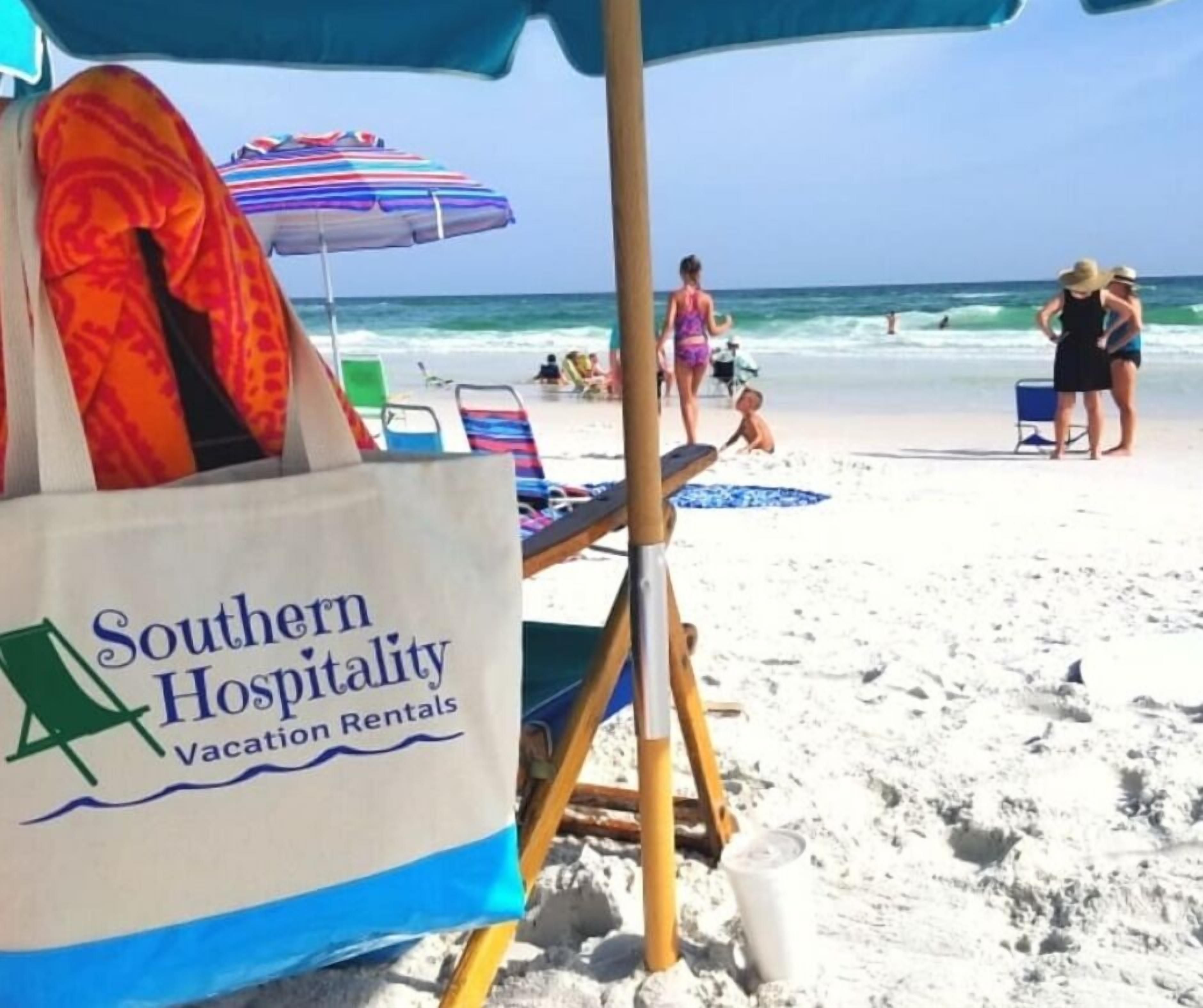 A beach scene with a rental chair and umbrella, a beach chair, and a sign for Southern Hospitality Vacation Rentals.