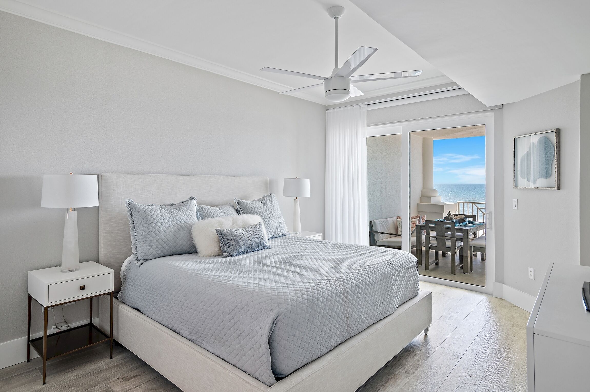 A bedroom with a bed, nightstands, a ceiling fan, and a view of the outdoors.