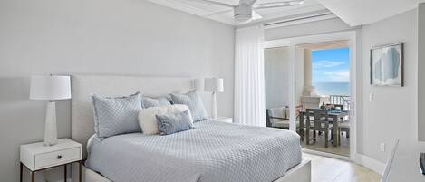A bedroom with a bed, nightstands, a ceiling fan, and a view of the outdoors.