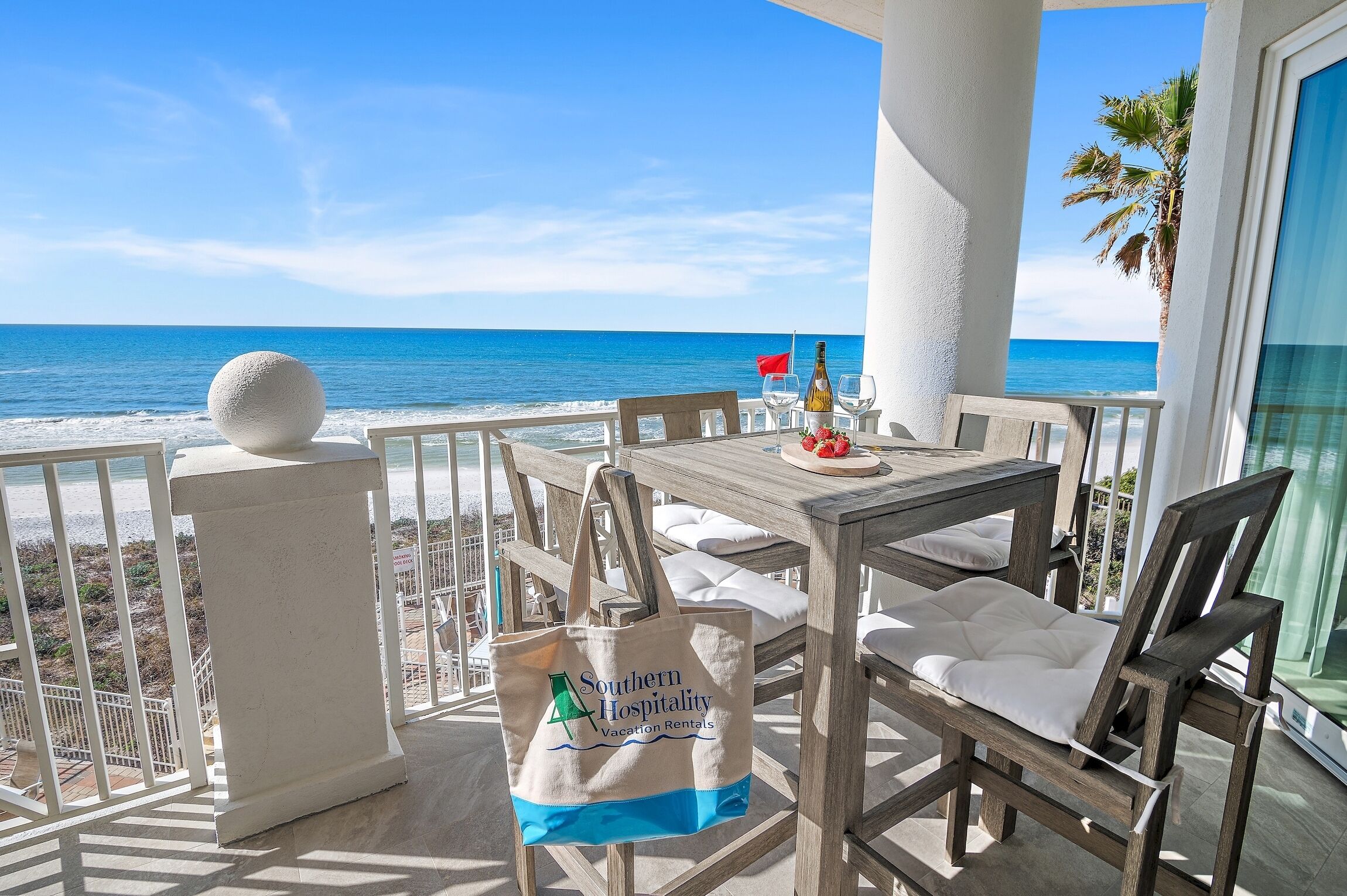 A wooden table with a bottle and glasses, a white cushion, and a Southern Hospitality Vacation Rentals tote bag.