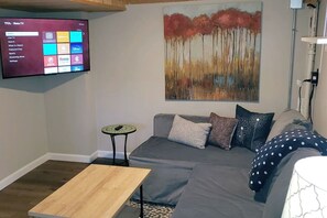 A modern living room with a grey sofa, a small wooden coffee table, and a flat-screen TV mounted on the wall displaying a Roku interface. - B-town Hideaway (Bloomington)