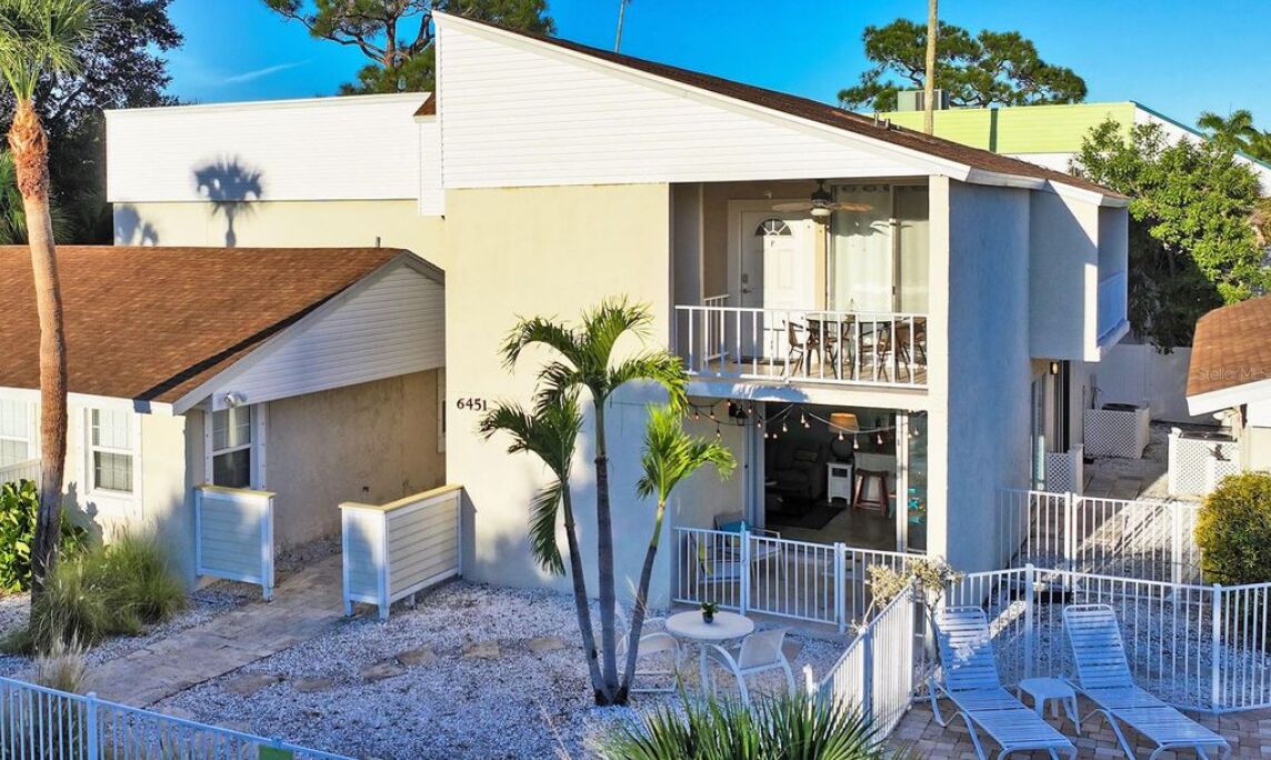 A two-story house with a balcony, a patio with chairs, and a small garden area.
