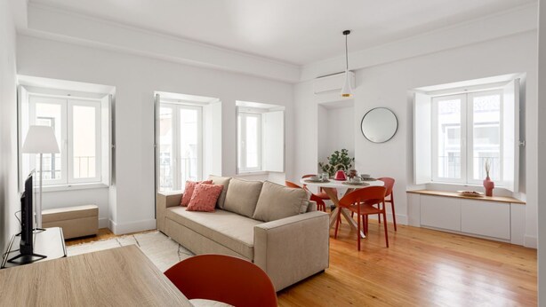 Un salon moderne comprenant un canapé, une table à manger et des chaises. De grandes fenêtres laissent entrer la lumière naturelle.