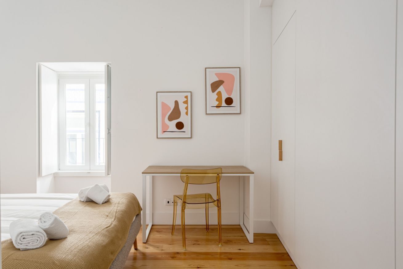 Ein minimalistisches Schlafzimmer mit einem Bett, einem Schreibtisch und zwei abstrakten Kunstwerken an der Wand.