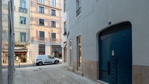 A narrow cobblestone street with a white van parked on the side, buildings with balconies, and a blue door on the right. - JOIVY Central deluxe flat (Lisbon)