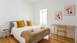 A bedroom with a bed, bedside table, chair, desk, and artwork. - JOIVY Central deluxe flat (Lisbon)