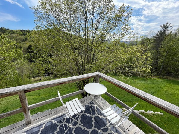 Una terraza de madera con una mesa y sillas, con vista a un área verde con árboles.