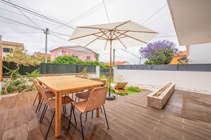 Un patio al aire libre con una mesa y sillas de madera, un paraguas grande y una jardinera de piedra.
