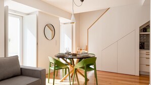 A modern dining area with a round table, green chairs, and a white pendant light. - JOIVY Splendid downtown penthouse (Lisbon)