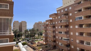 A multi-story residential building with balconies, a courtyard with palm trees, and a clear blue sky.