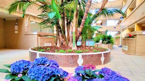 A circular planter with a palm tree and hydrangeas in a hotel atrium.