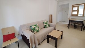 A living room with a sofa, a small table, a chair, and a dining area with a table and chairs. - ACV - Vistamar Iii-1ª Linea Planta 2 Norte 2 (OROPESA)