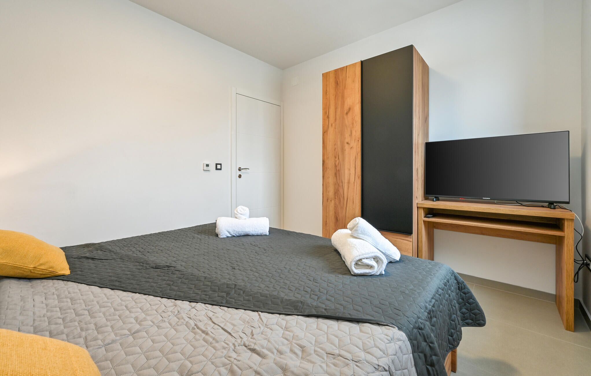 Una habitación de hotel con cama, televisor sobre un soporte de madera y armario.