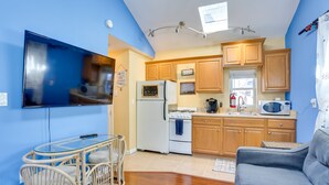 A compact kitchen with wooden cabinets, a refrigerator, stove, microwave, and a dining area with a glass table and chairs. - Greenwood Lake Cottage w/ Shared Dock & Hot Tub! (Hewitt)