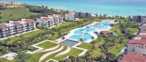 Un resort con múltiples piscinas, una gran piscina central y vista al océano.