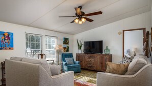 A living room with two armchairs, a blue sofa, a wooden cabinet with a TV, and a ceiling fan.