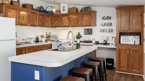 A modern kitchen with wooden cabinets, a central island with stools, a microwave, and various kitchen appliances.