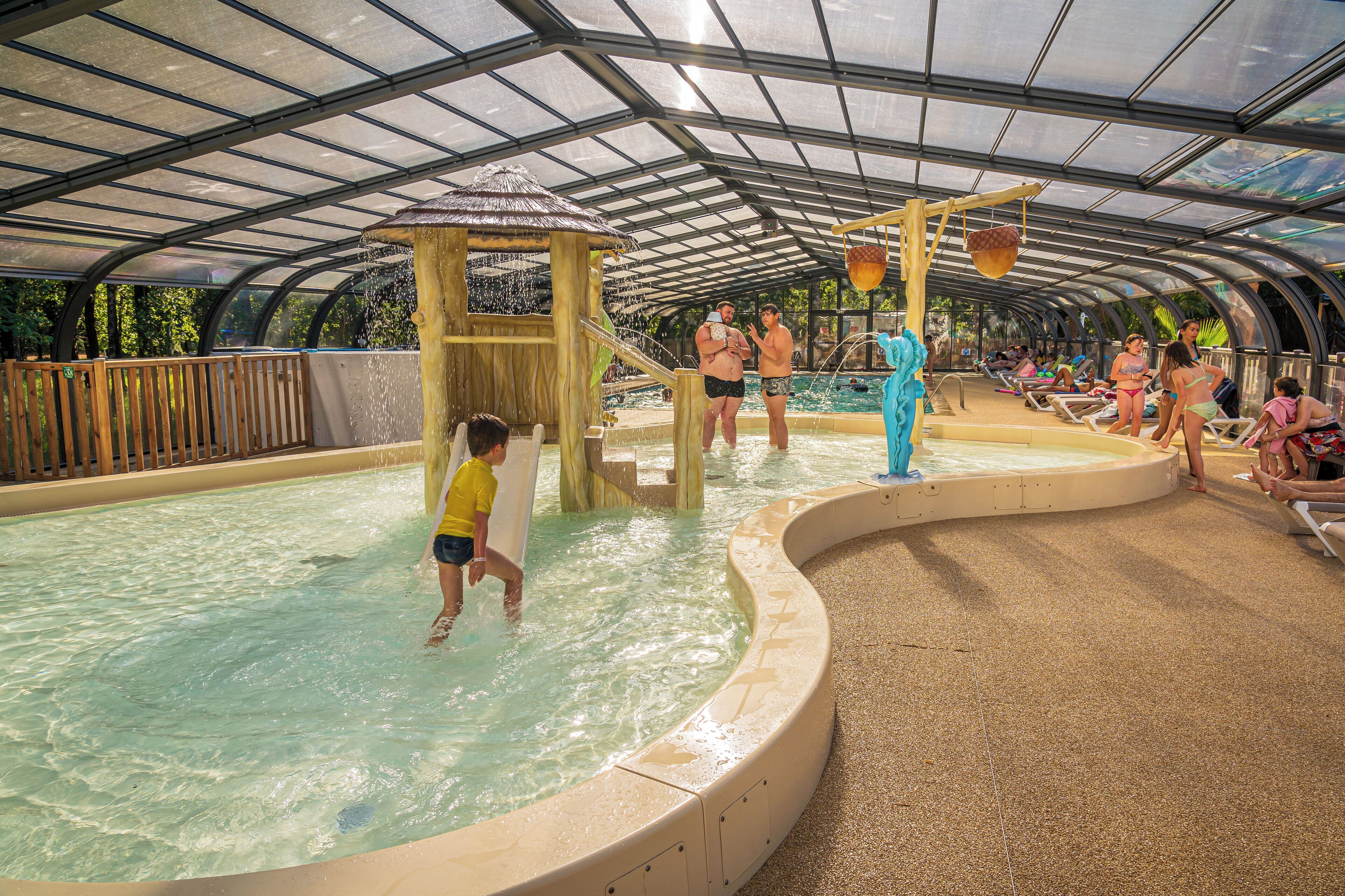 An indoor water park with a covered area, a pool, and a play structure.