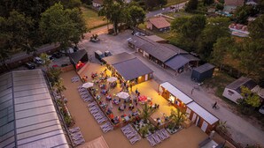 An outdoor seating area with tables and chairs, surrounded by buildings and trees. - Proche Lac & Océan | Piscine | Camping 4* (Hourtin)