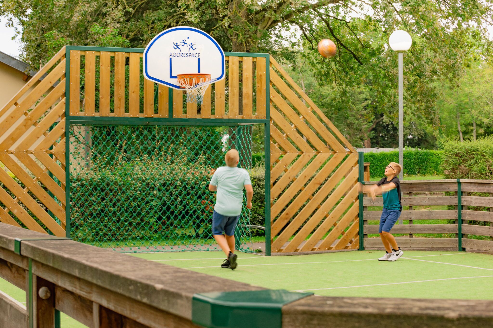 Un terrain de basket en plein air, entouré d’une clôture en bois et équipé d’un panier de basket.