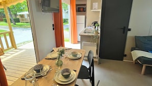 Comedor con mesa de madera dispuesta para dos personas, televisor montado en la pared y zona de cocina con microondas y refrigerador.