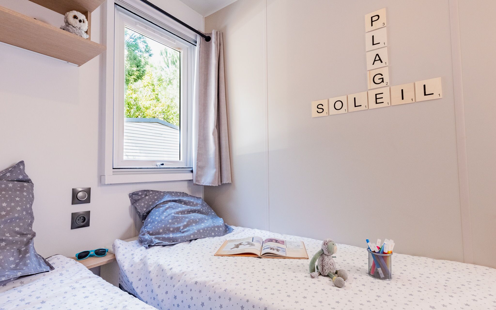 A bedroom with a bed, a window, and a wall with Scrabble tiles spelling "PLAG SLEIL".