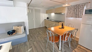 A compact kitchen with a dining table, chairs, a refrigerator, and a microwave. - Chalet Tulum TV Clim - 2 chambres - 4 personnes (Le Muy)