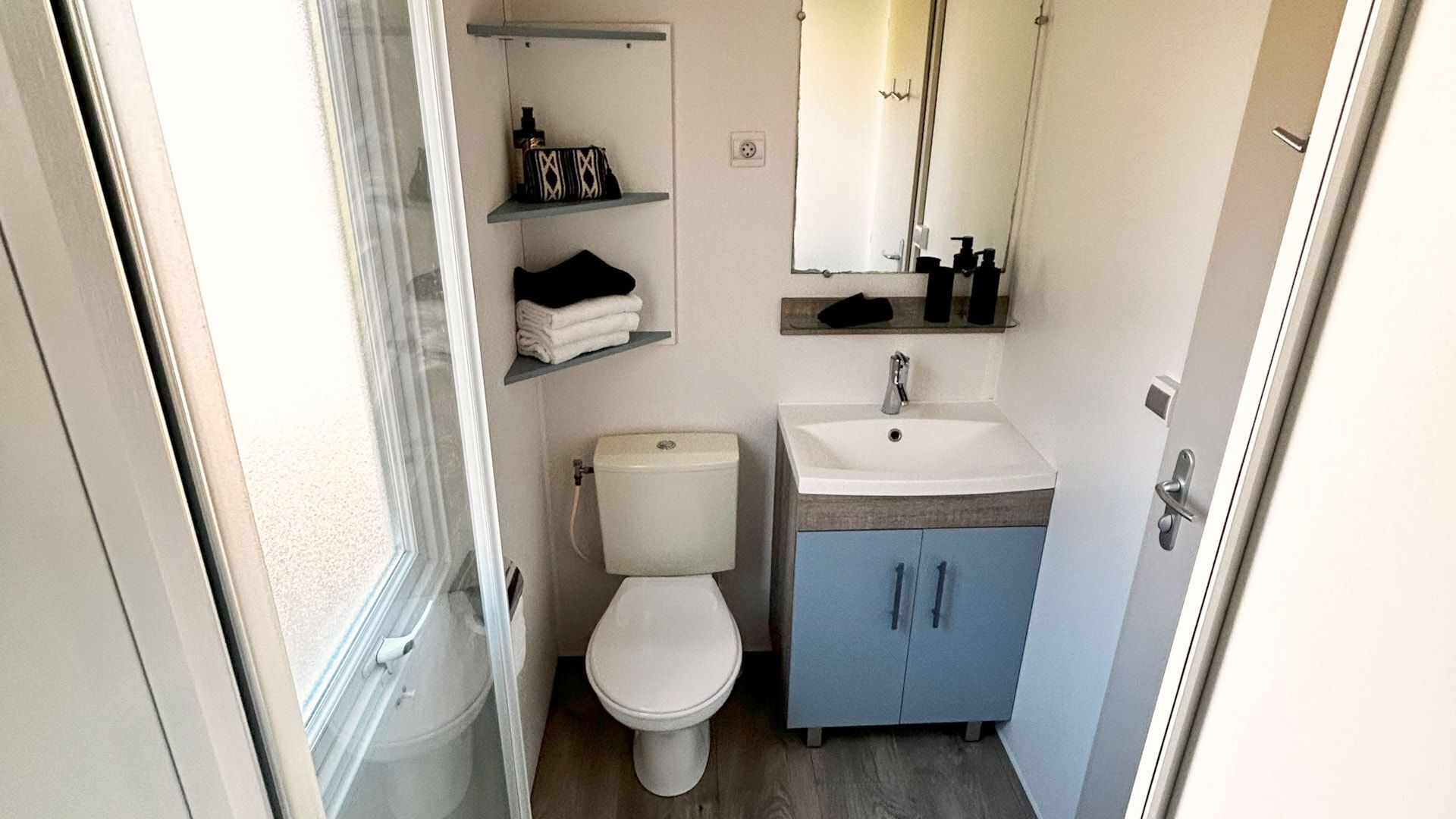 Un baño pequeño con inodoro, lavamanos y estantes para guardar objetos.