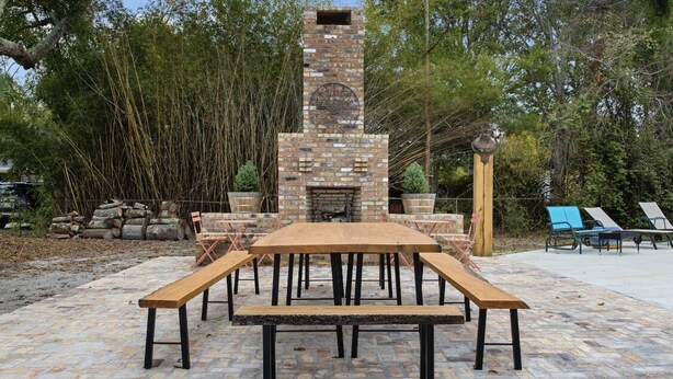 Eine Terrasse im Freien mit einem Kamin aus Ziegelsteinen, Holzbanken und einem Tisch.