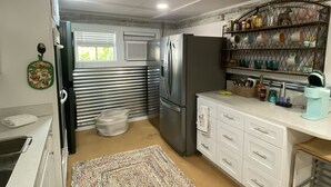 Eine kompakte Küche mit weißen Schränken, einem Edelstahlkühlschrank, einer Kaffeemaschine und einem gemusterten Teppich.