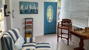 Una sala de estar acogedora con un sofá a rayas, una mesa de ajedrez, una estantería, una puerta con un panel azul y una pintura de un velero.