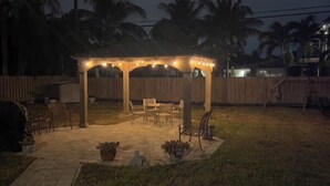 Un área de patio techada con luces colgantes, un banco de madera y una mesa.