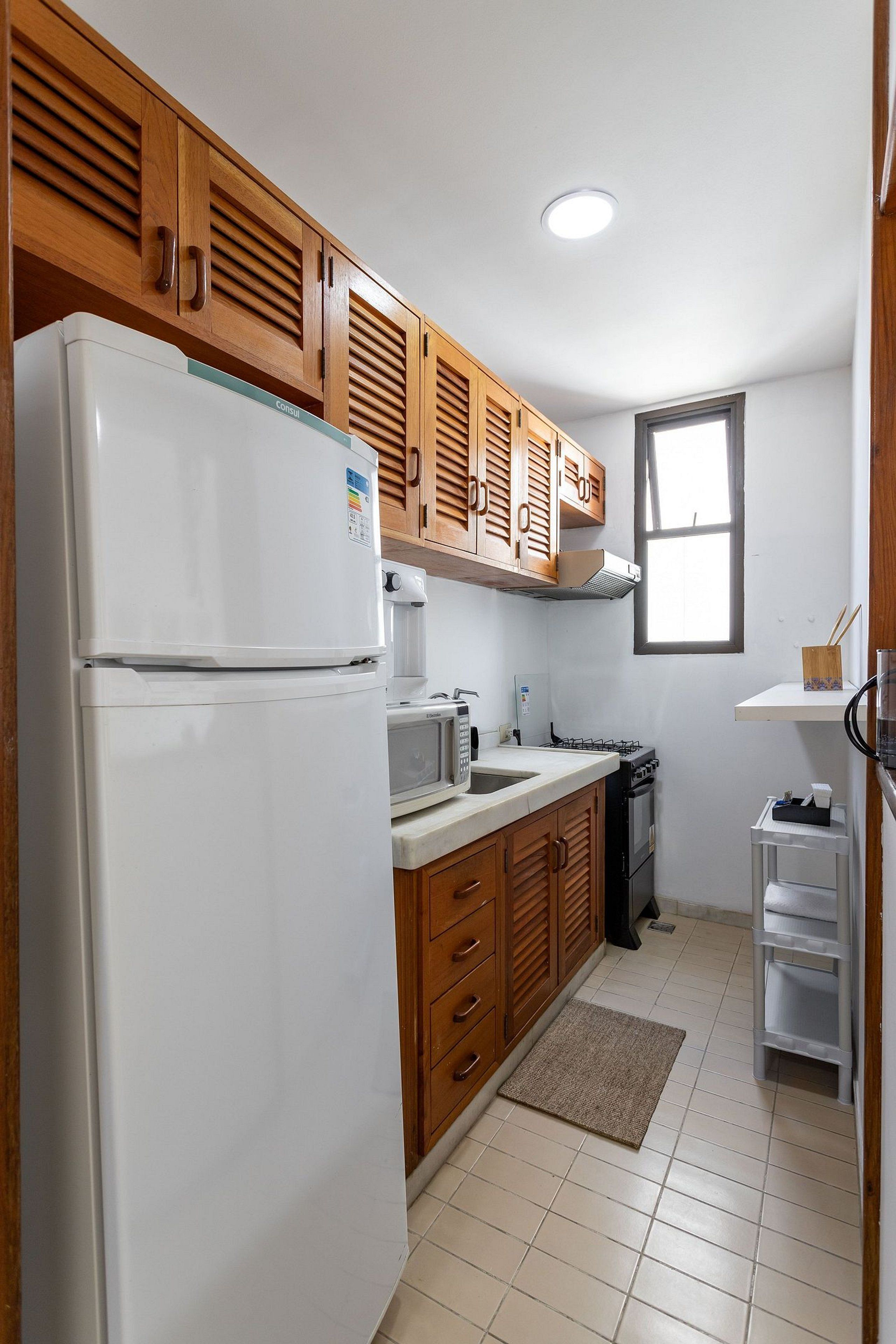 A compact kitchen with wooden cabinets, a white refrigerator, a microwave, and a gas stove.